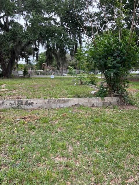 A grassy, vacant lot features a low concrete block retaining wall and mature trees — 3799 AVENUE T NW, WINTER HAVEN, FL