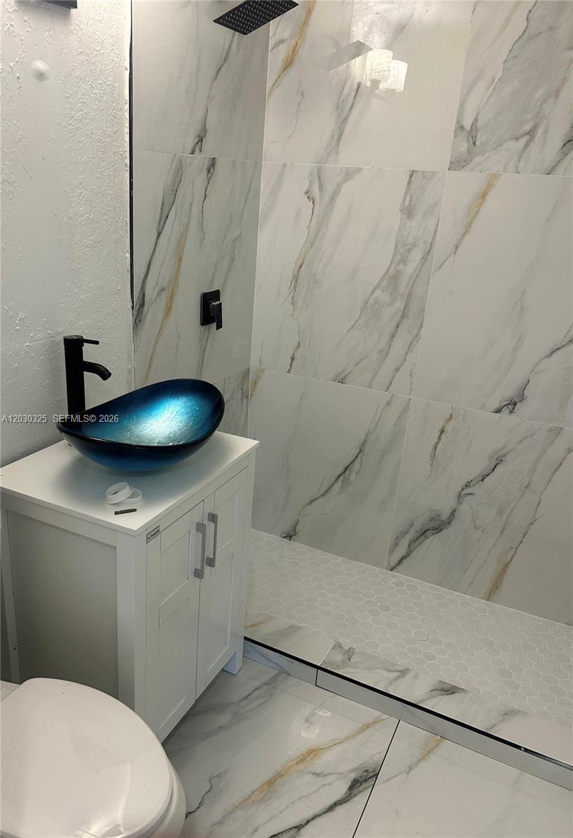 A bathroom features a white vanity, a blue vessel sink, and marble-patterned wall tiles — 4125 SW 108th Ct, Miami FL 33165, MIAMI, FL