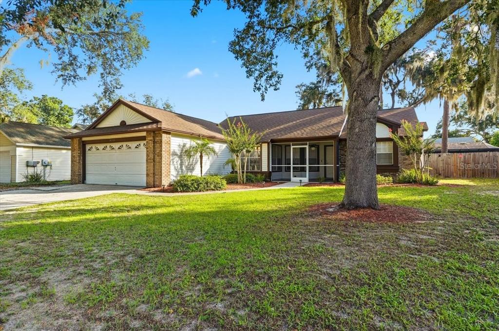 A single-story house with a white garage, brick accents, and a large tree in front — 4110 LONGFELLOW DRIVE, PLANT CITY, FL