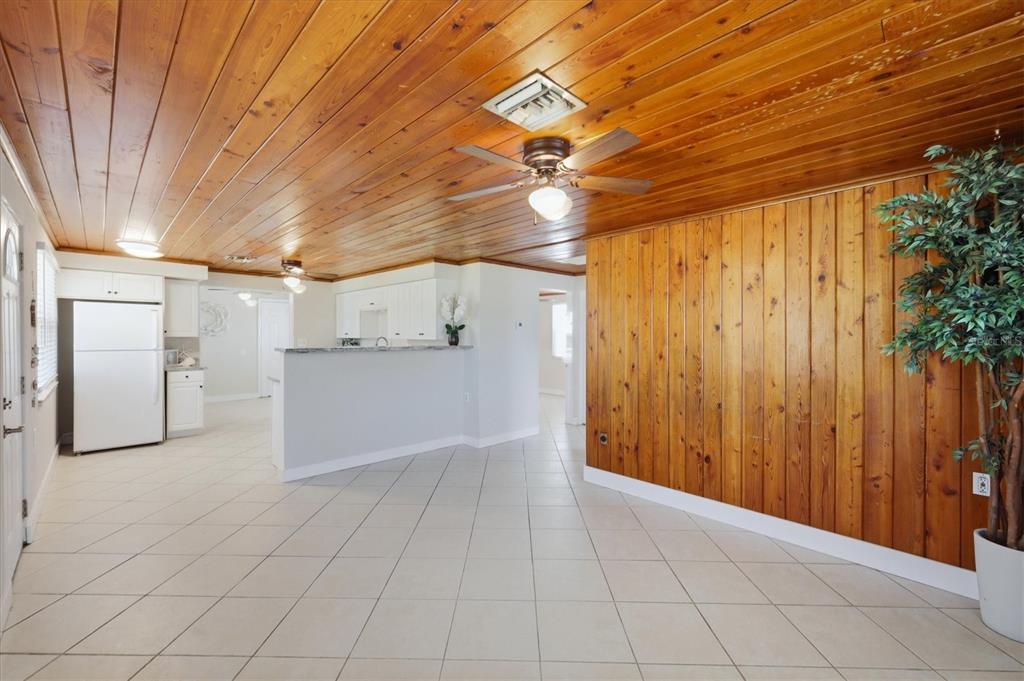 A kitchen and living area featuring wood-paneled walls, a wood ceiling, and light tile flooring — 155 MAGNOLIA AVENUE, ENGLEWOOD, FL