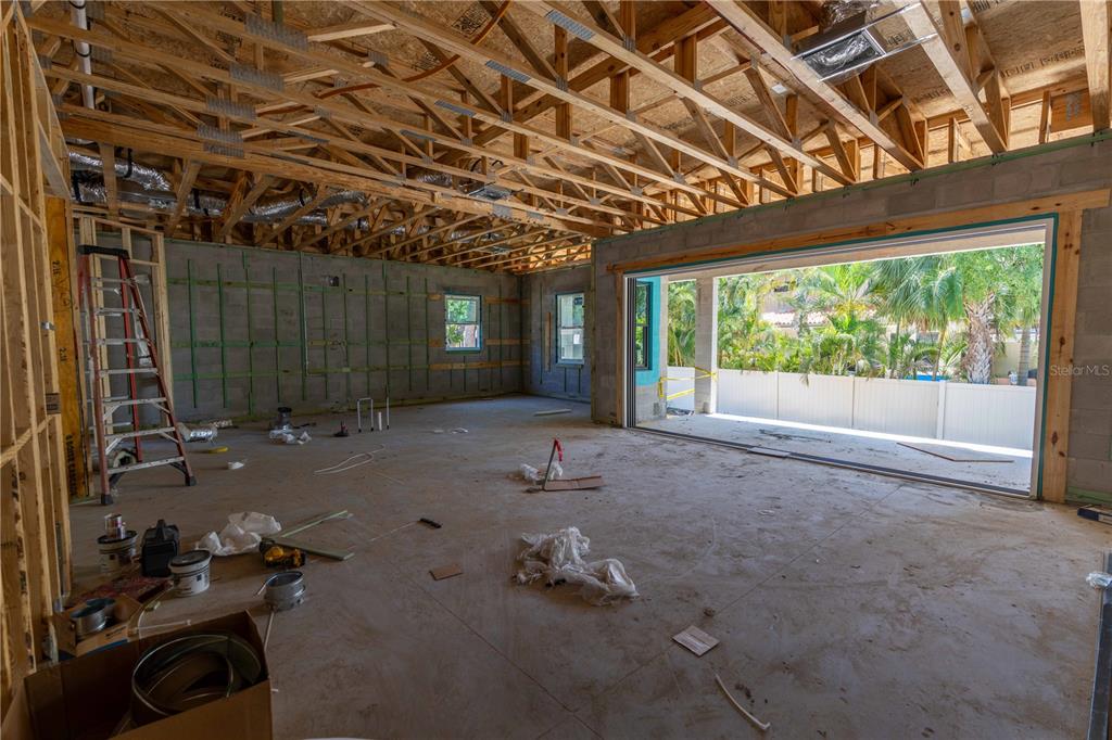 An unfinished room with exposed wood trusses, concrete block walls, and large sliding glass doors — 4316 W CORONA STREET, TAMPA, FL