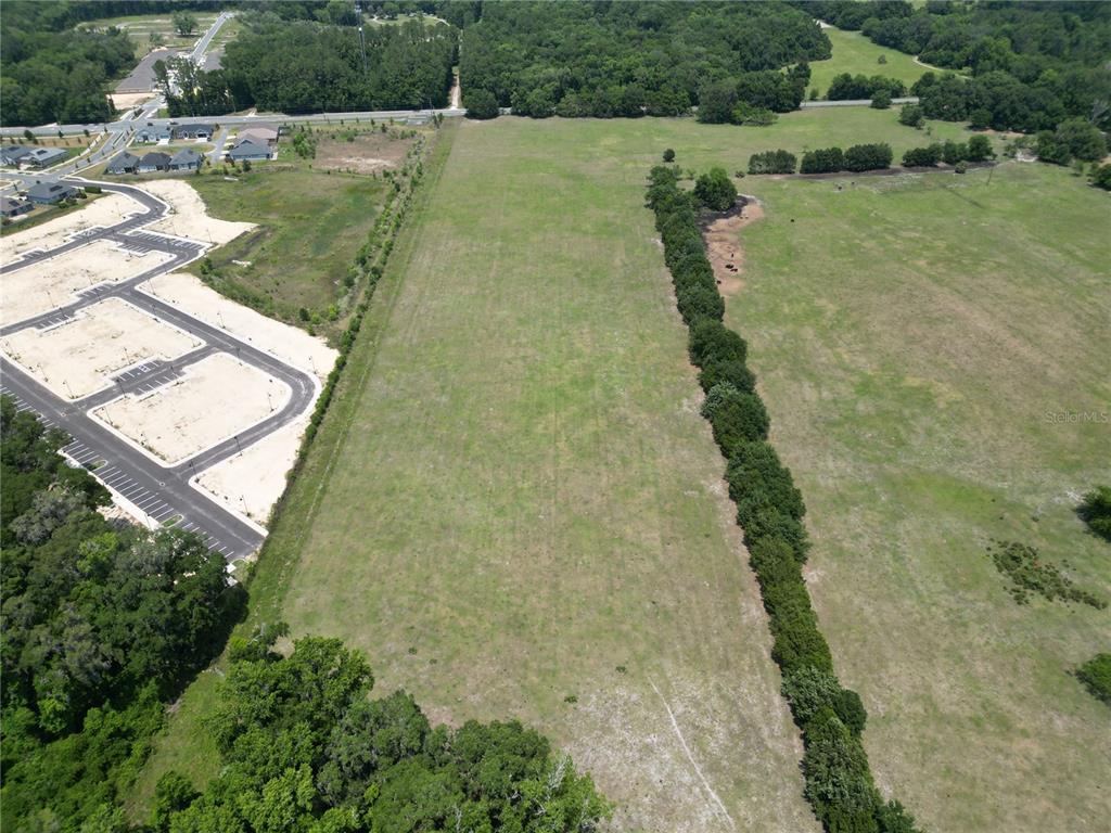 An aerial view shows a large, grassy vacant lot adjacent to a new residential development — 24.11 Acres SW 62ND AVENUE, GAINESVILLE, FL