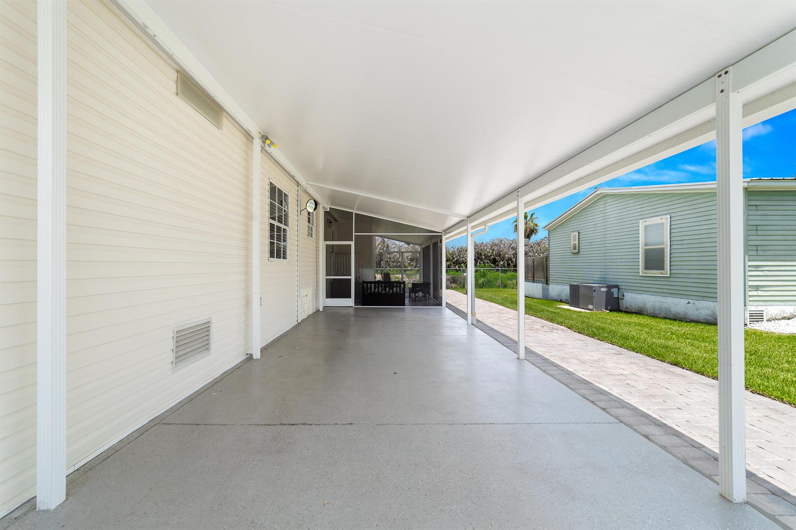 A covered concrete patio extends alongside a light-colored home with a screened-in porch area — 1637 SW 35th Circle, Okeechobee FL 34974, OKEECHOBEE, FL