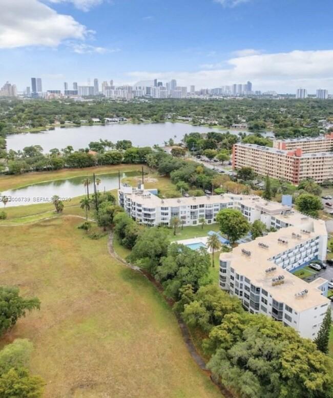 An aerial view shows multi-story apartment buildings, a swimming pool, and a lake near a city — 1701 NE 191st St # A106, Miami FL 33179, MIAMI, FL