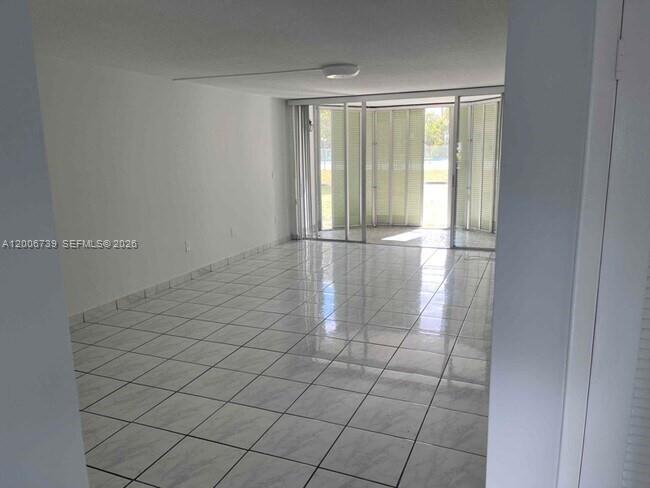 An empty room with white tiled floors and a large sliding glass door to outside — 1701 NE 191st St # A106, Miami FL 33179, MIAMI, FL