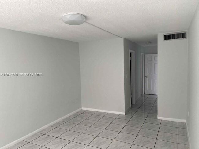 An empty room with light gray walls, white tile flooring, and a ceiling-mounted light fixture — 1701 NE 191st St # A106, Miami FL 33179, MIAMI, FL