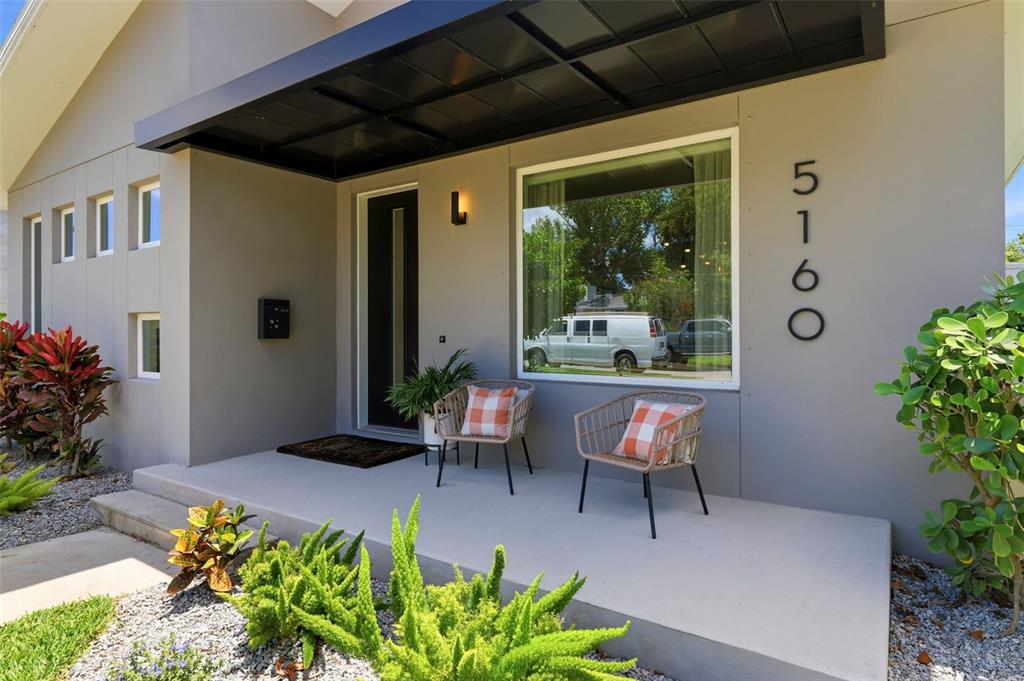 The exterior of a modern home features a covered porch with two chairs and landscaping — 5160 DARTMOUTH AVENUE N, ST PETERSBURG, FL