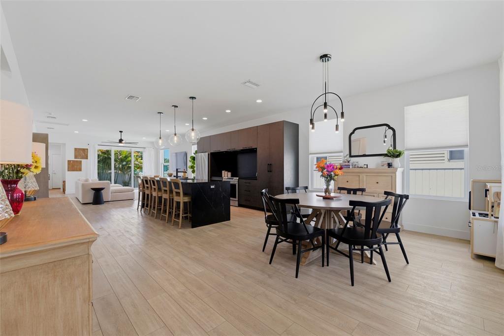 An open-concept kitchen and dining area features dark cabinetry, a black island, and wood flooring — 5160 DARTMOUTH AVENUE N, ST PETERSBURG, FL