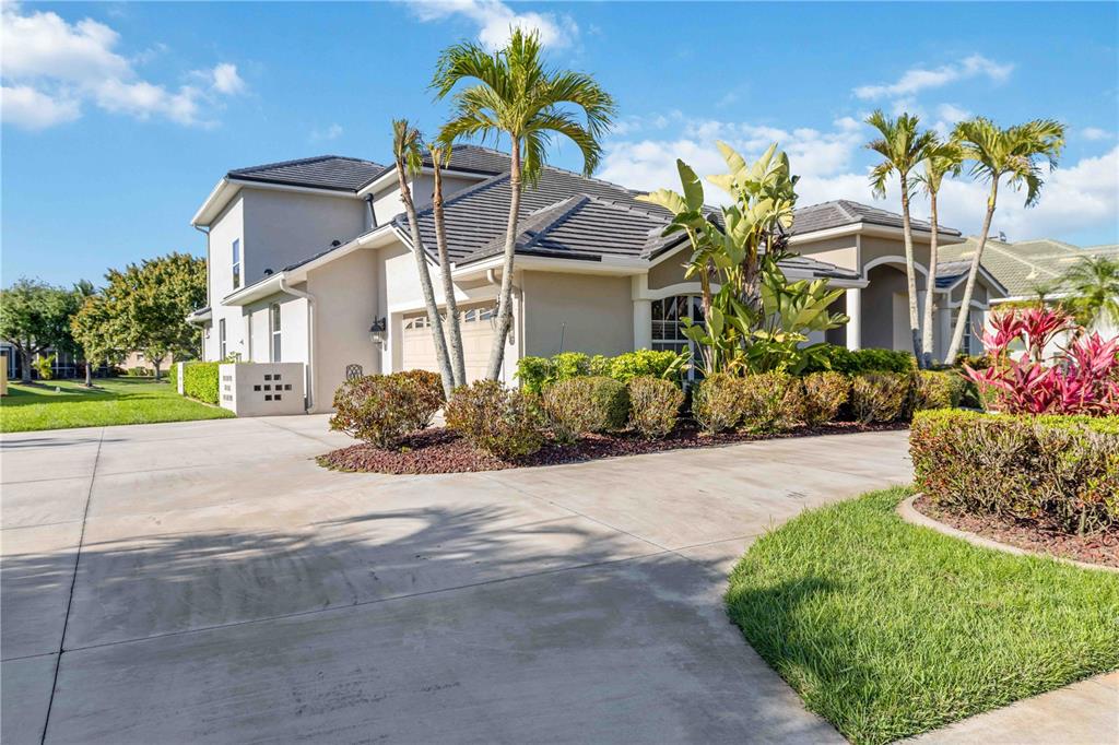 A two-story house with a concrete driveway, palm trees, and landscaping under a blue sky — 8335 BARTON FARMS BOULEVARD, SARASOTA, FL