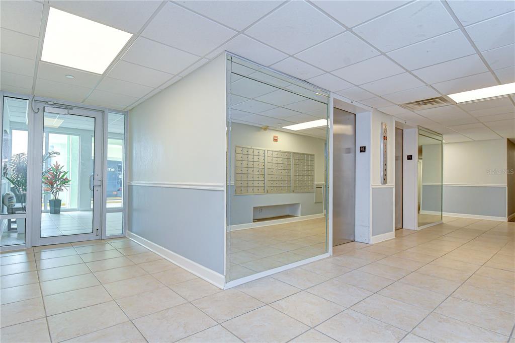 A lobby area features tiled floors, a mirrored wall with mailboxes, and two elevator doors — 400 64TH AVENUE UNIT 1006, ST PETE BEACH, FL