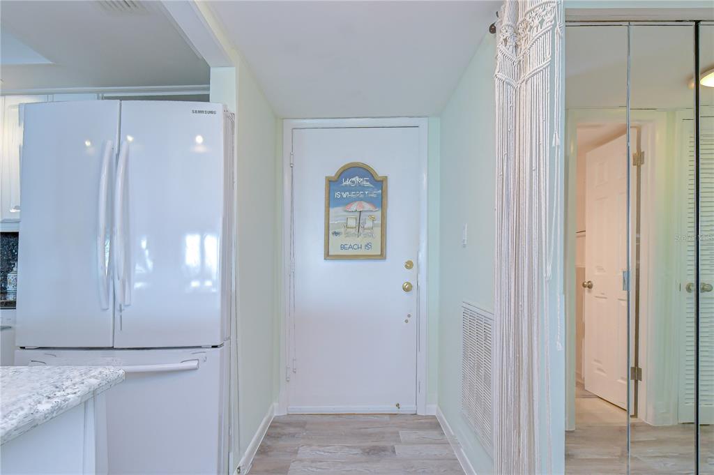 A white refrigerator stands next to an entrance door with a beach-themed wall sign — 400 64TH AVENUE UNIT 1006, ST PETE BEACH, FL