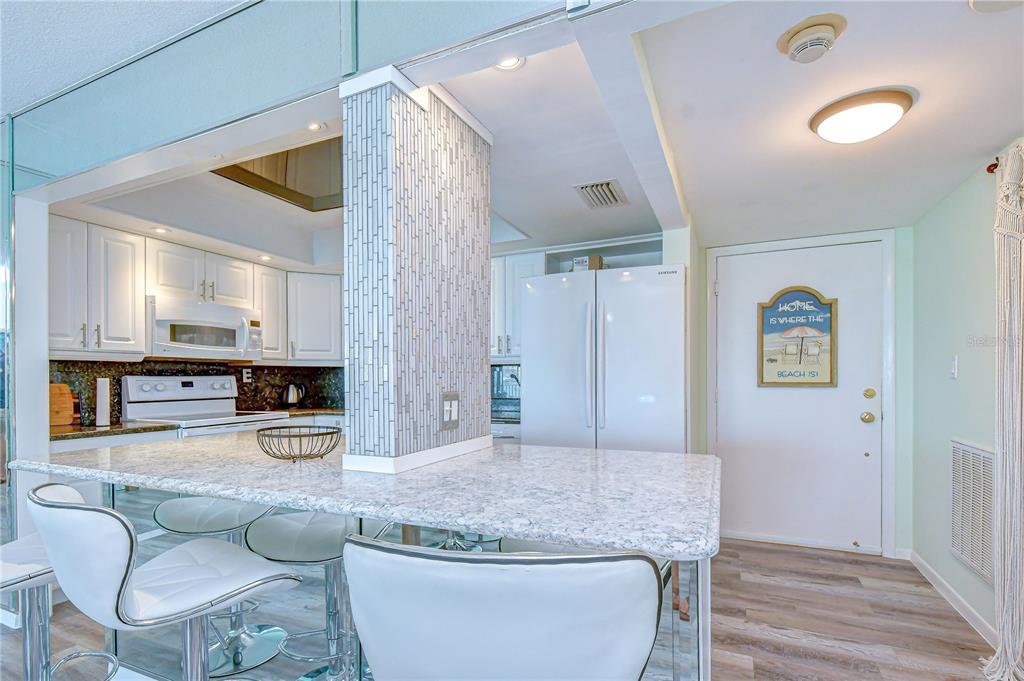 A kitchen with white cabinets, granite countertops, a breakfast bar, and a white refrigerator — 400 64TH AVENUE UNIT 1006, ST PETE BEACH, FL