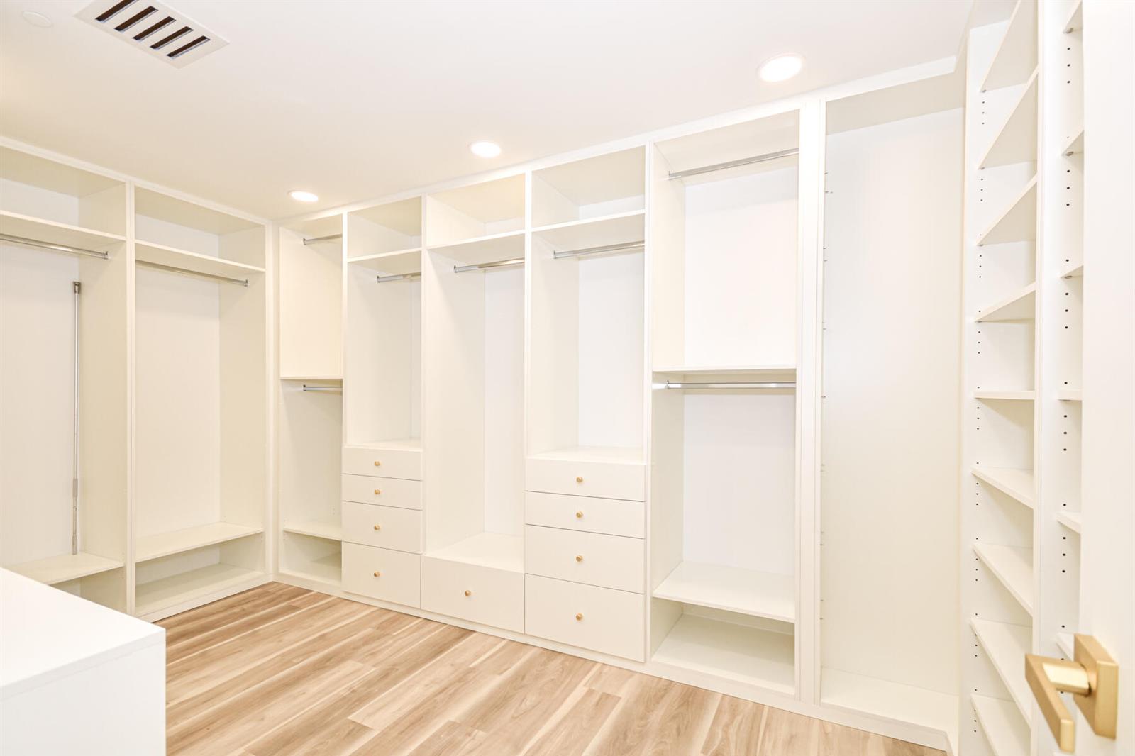 A walk-in closet features white built-in shelving, hanging rods, drawers, and light wood flooring — 10101 Collins Avenue # 7d, Bal Harbour FL 33154, BAL HARBOUR, FL