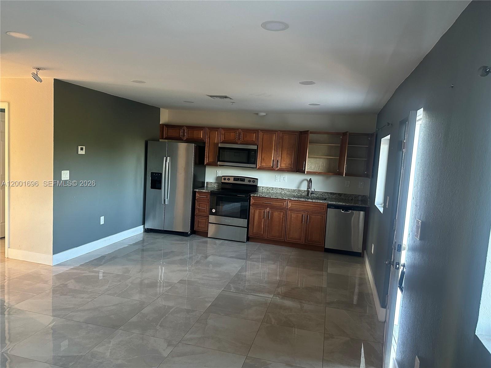 A kitchen features wood cabinets, stainless steel appliances, granite countertops, and large gray floor tiles — 587 NW 100th St # C, Miami FL 33150, MIAMI, FL