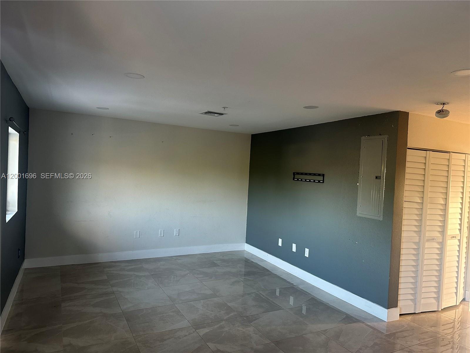 An empty room features gray tile flooring, a dark accent wall, and a circuit breaker panel — 587 NW 100th St # C, Miami FL 33150, MIAMI, FL