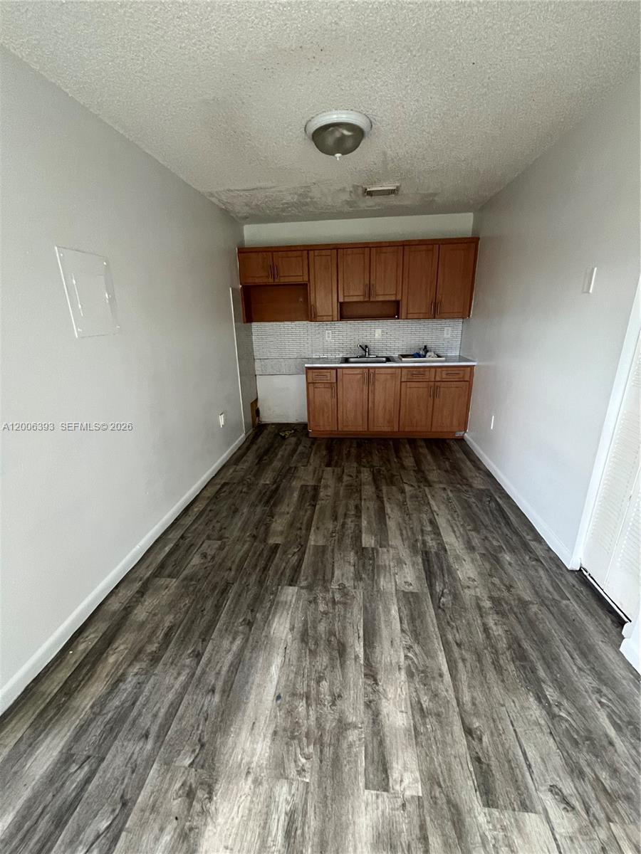 A small kitchen area features wood cabinets, a white backsplash, and dark wood-look flooring — 334 E 21st St # 3, Hialeah FL 33010, HIALEAH, FL