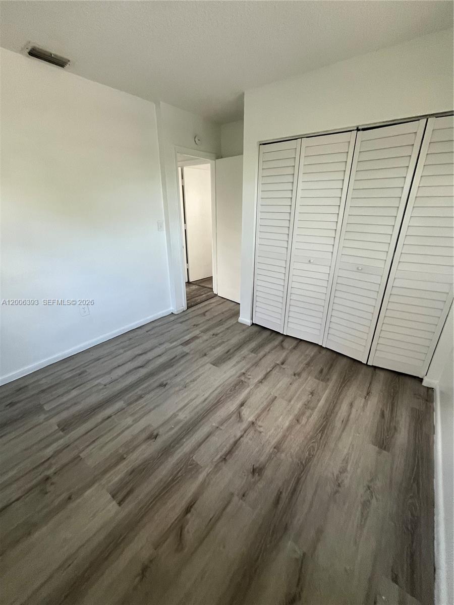 An empty bedroom features wood-look flooring, white walls, and a white louvered closet door — 334 E 21st St # 3, Hialeah FL 33010, HIALEAH, FL