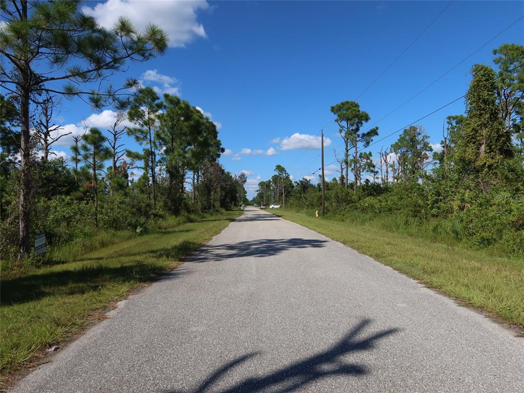 A paved road stretches through a wooded area under a blue sky with scattered clouds — 8178 DIMSTEAD STREET, PORT CHARLOTTE, FL