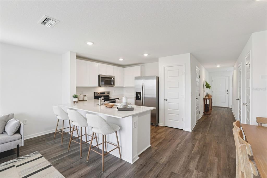 A modern kitchen features white cabinetry, stainless steel appliances, and a quartz-topped island with stools — 4351 BUTTERSCOTCH CIRCLE, LAKELAND, FL