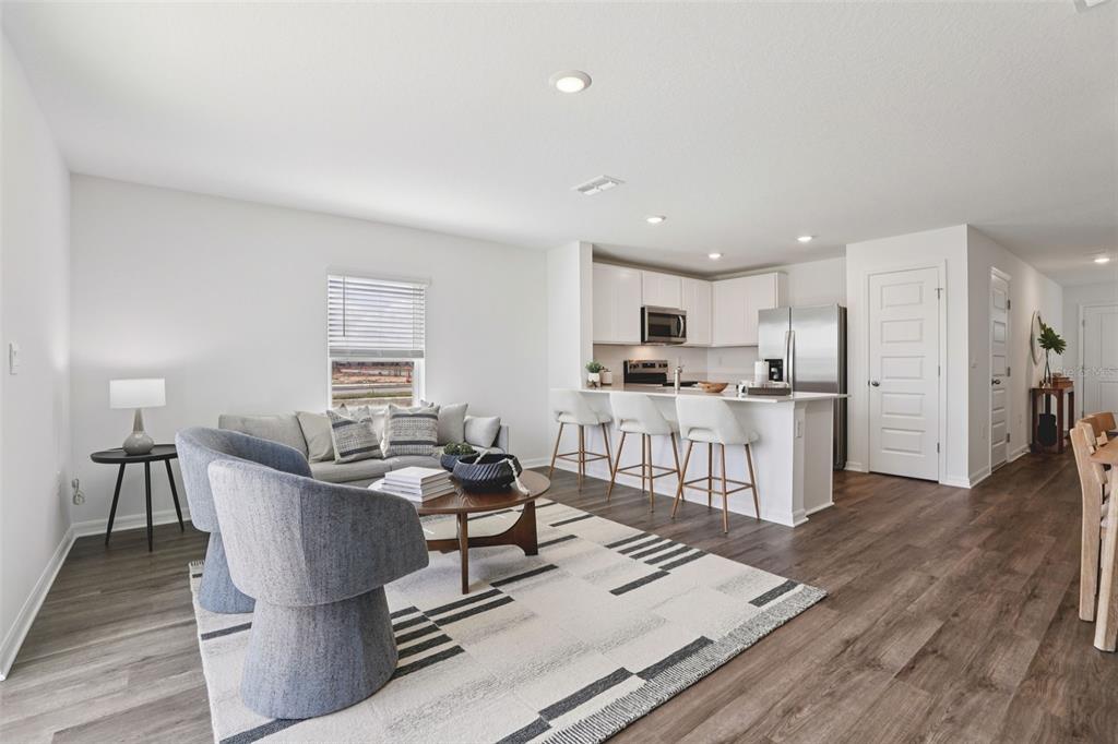 An open-concept living room and kitchen featuring white cabinetry, a breakfast bar, and wood flooring — 4351 BUTTERSCOTCH CIRCLE, LAKELAND, FL