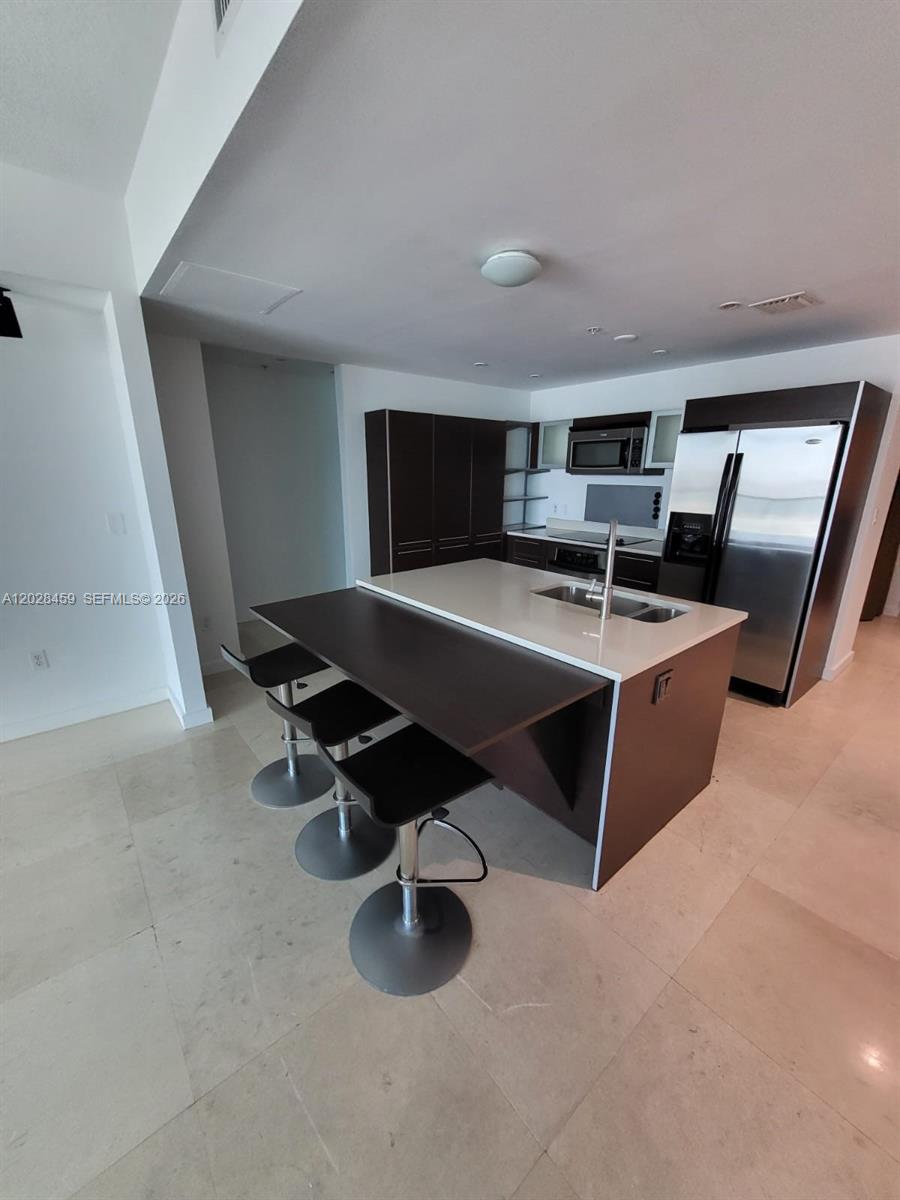 A modern kitchen features dark cabinetry, a white quartz island, and three bar stools — 1900 N Bayshore Dr # 2415, Miami FL 33132, MIAMI, FL