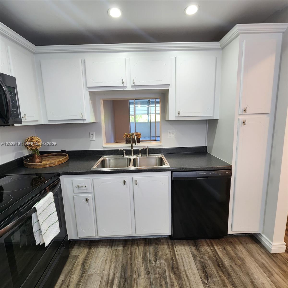 A kitchen features white cabinets, black countertops, black appliances, and wood-look flooring — 900 NE 12th Ave # 406, Hallandale Beach FL 33009, HALLANDALE BEACH, FL