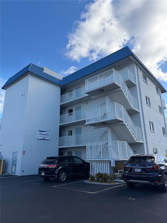 A multi-story apartment building with exterior staircases and two parked cars in the foreground — 800 BAYWAY BOULEVARD UNIT 16, CLEARWATER BEACH, FL