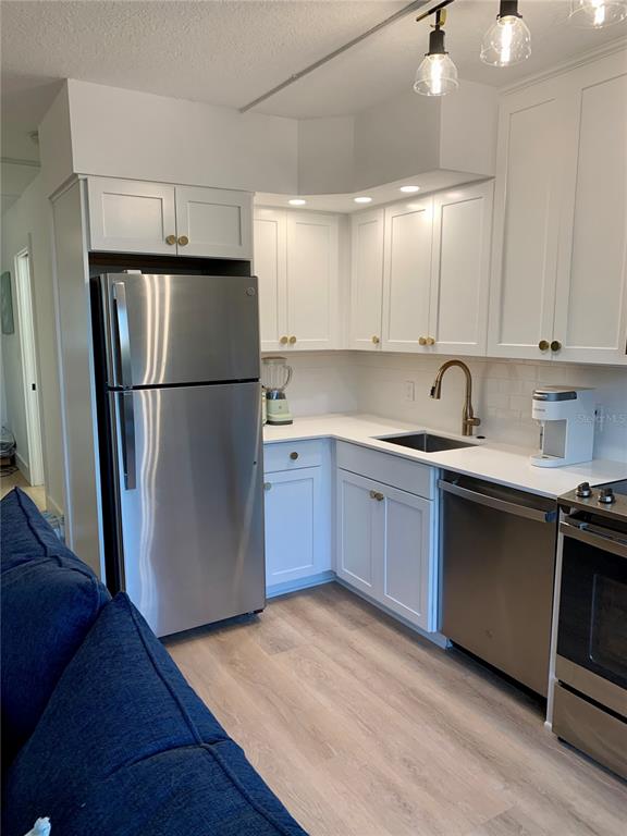 A kitchen features white cabinets, stainless steel appliances, a sink, and light wood-look flooring — 800 BAYWAY BOULEVARD UNIT 16, CLEARWATER BEACH, FL