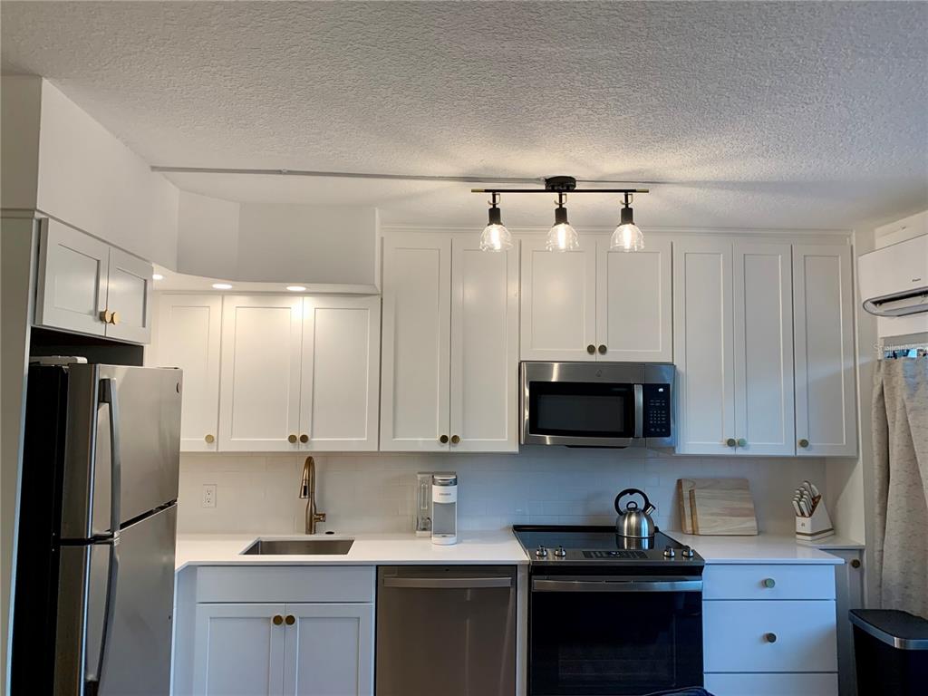 A kitchen features white cabinets, stainless steel appliances, a sink, and a three-light ceiling fixture — 800 BAYWAY BOULEVARD UNIT 16, CLEARWATER BEACH, FL