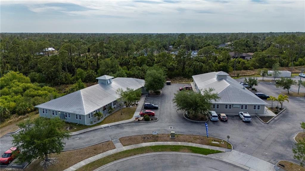 An aerial view shows two commercial buildings with metal roofs surrounded by parking and trees — 2525 BOBCAT VILLAGE CENTER ROAD, NORTH PORT, FL