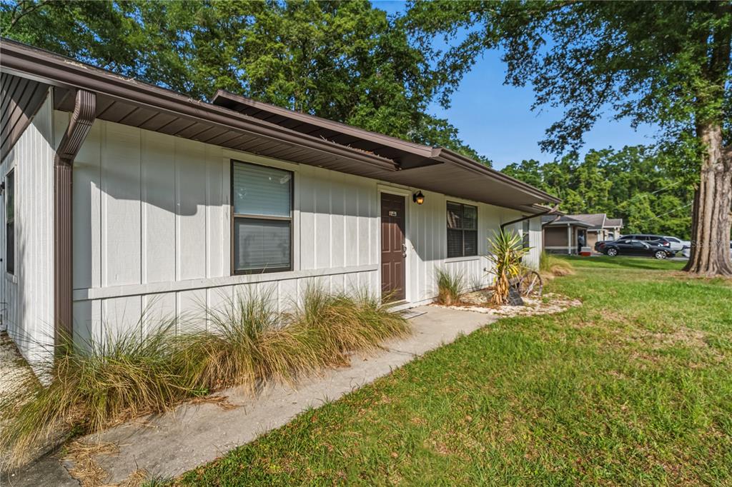 A single-story house with white vertical siding, a brown door, and a concrete walkway — 6915 NW 60TH STREET ROAD, OCALA, FL