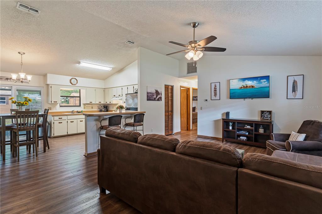 An open-concept living room and kitchen featuring wood-look flooring, a ceiling fan, and furniture — 6915 NW 60TH STREET ROAD, OCALA, FL