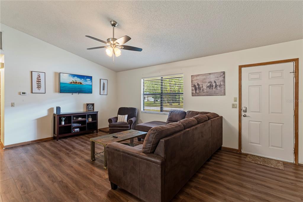 A living room features wood-look flooring, a brown sectional sofa, and a wall-mounted television — 6915 NW 60TH STREET ROAD, OCALA, FL
