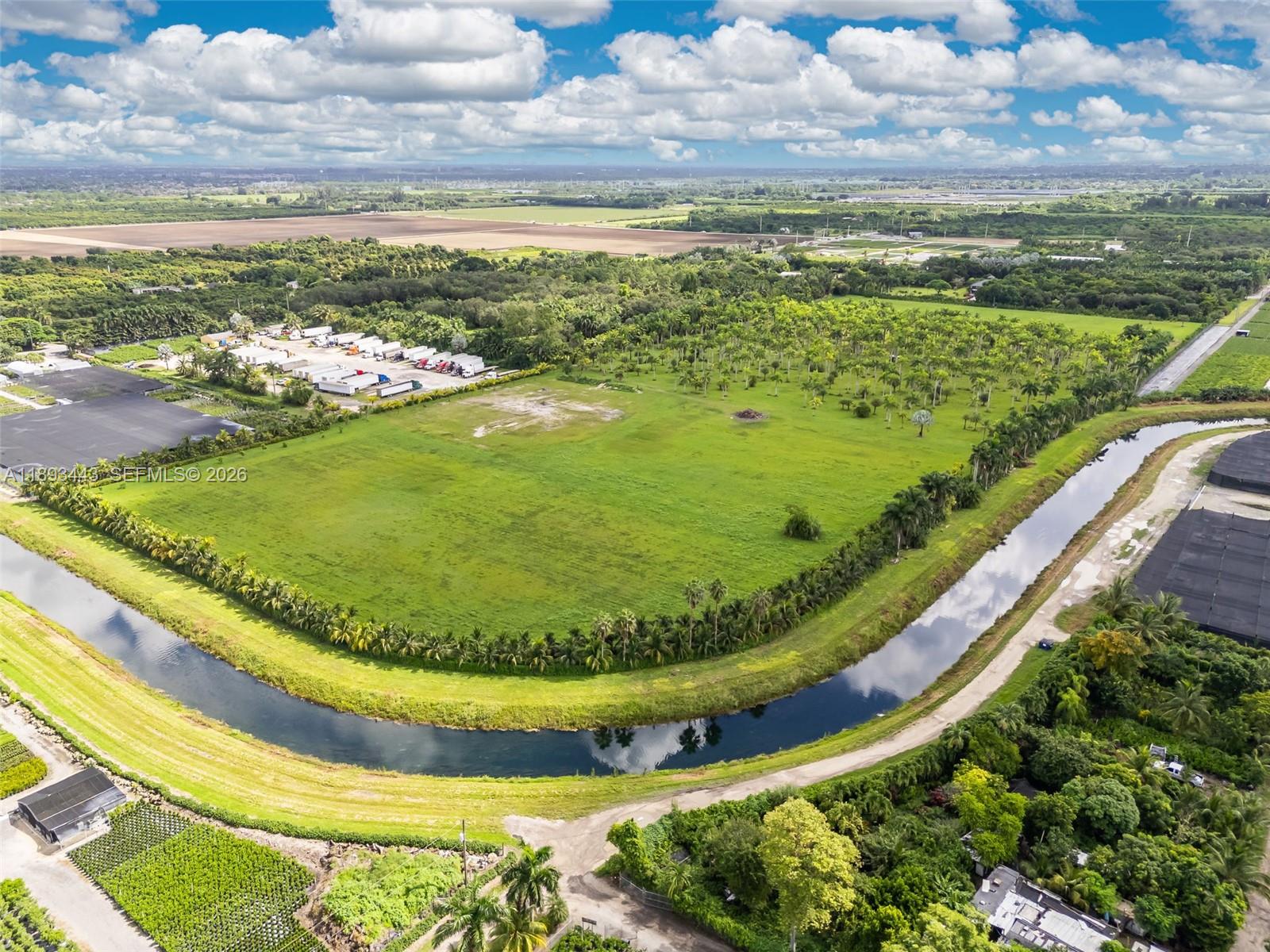 An aerial view shows a large green field bordered by a canal and palm trees — 15100 SW 200th St, Miami FL 33187, MIAMI, FL