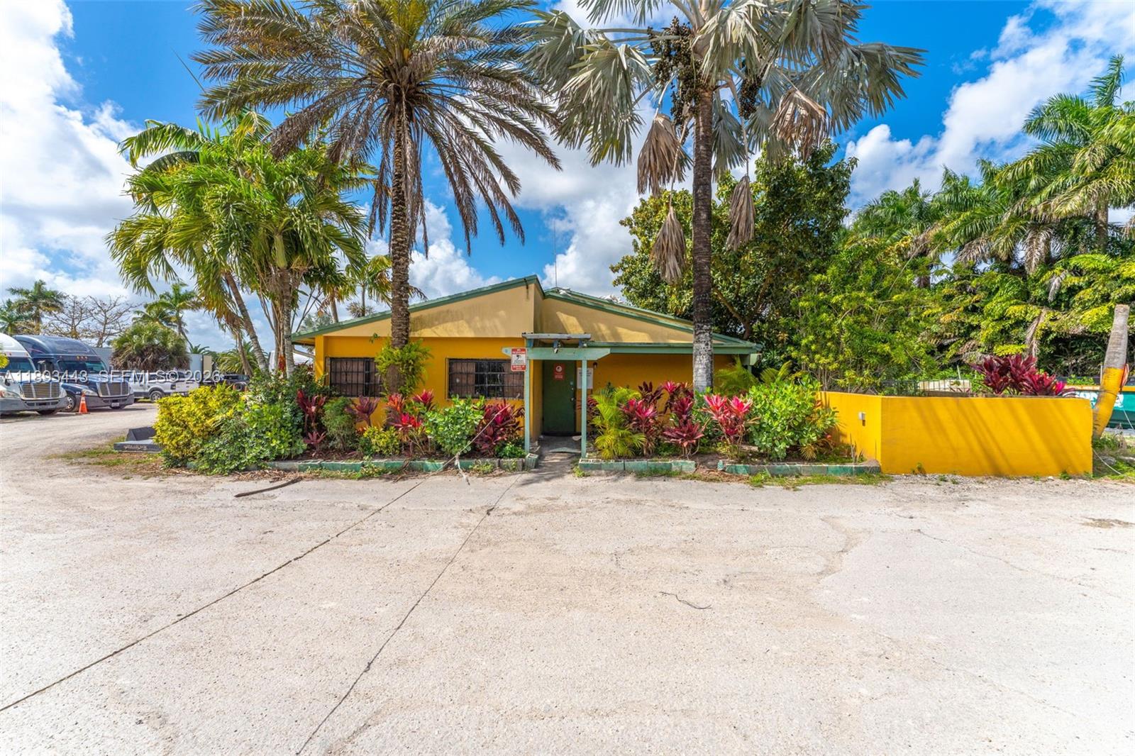 A yellow, single-story building stands behind a landscaped garden with palm trees and a parking lot — 15100 SW 200th St, Miami FL 33187, MIAMI, FL