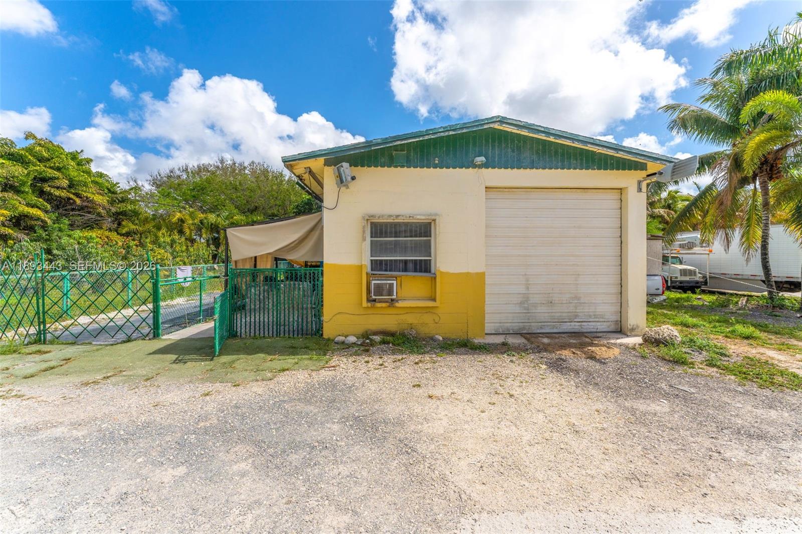 A yellow and white detached garage with a roll-up door sits on a gravel lot — 15100 SW 200th St, Miami FL 33187, MIAMI, FL