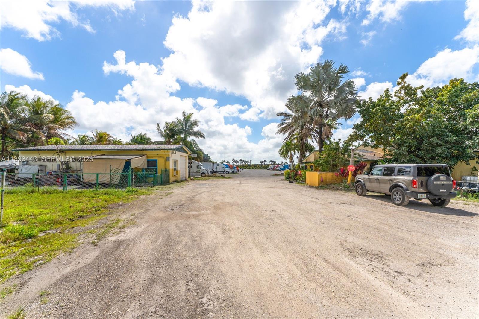 A dirt driveway leads past a yellow building and a parked SUV toward parked trucks — 15100 SW 200th St, Miami FL 33187, MIAMI, FL