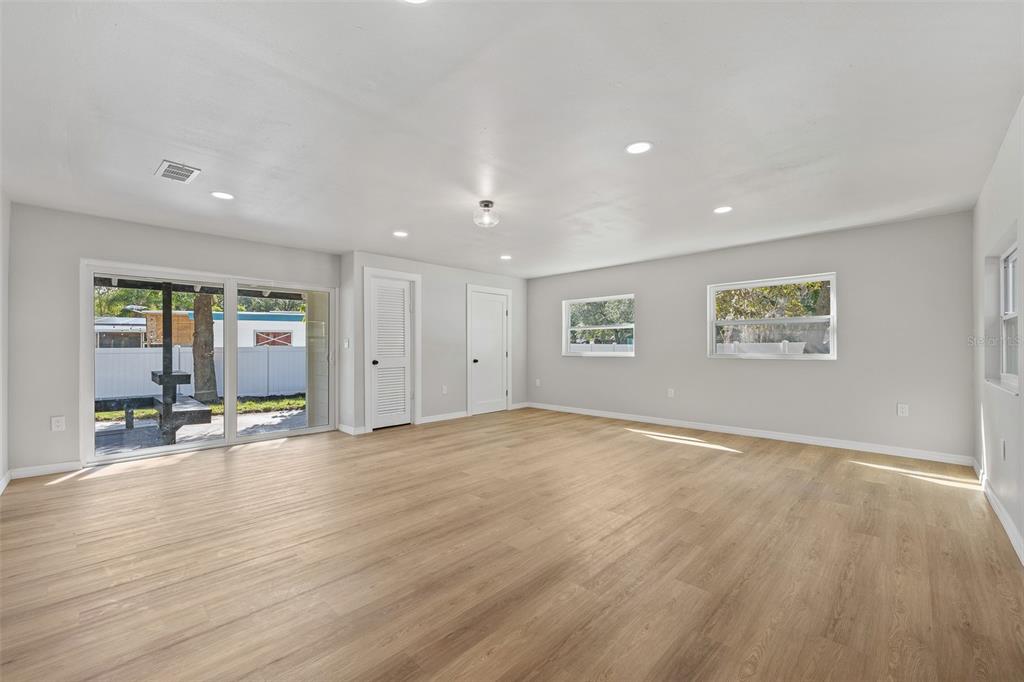 A bright, empty room features light wood-look flooring, recessed lighting, white walls, and sliding glass doors — 2800 E ANDERSON STREET, ORLANDO, FL