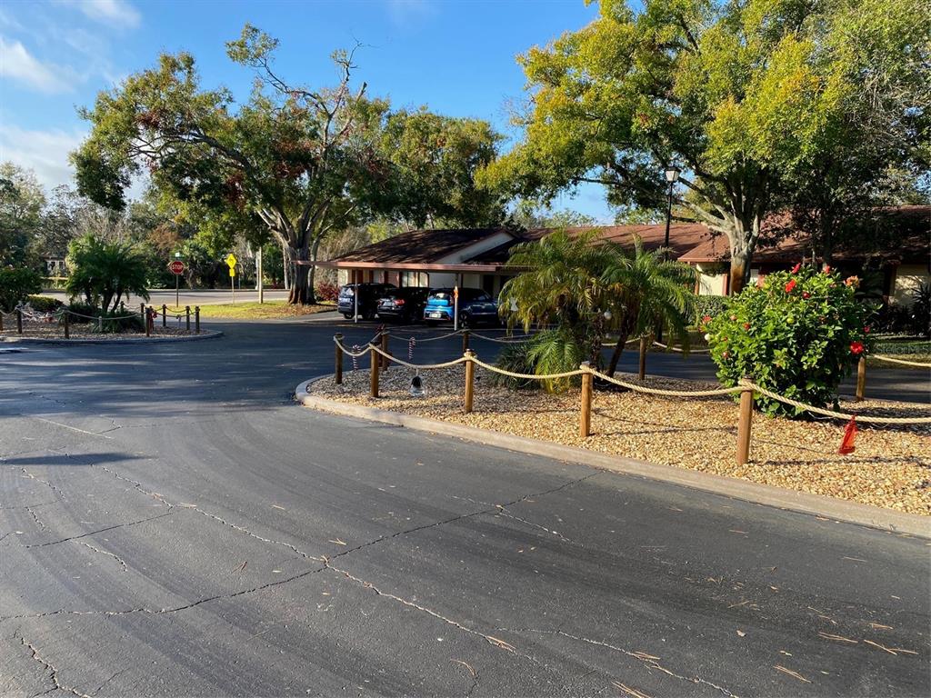 A paved driveway leads to a covered parking area beside a building with mature trees — 12539 GREYLOCK LANE, HUDSON, FL