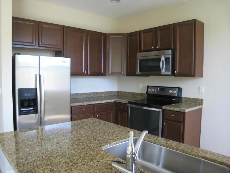 A kitchen features dark wood cabinets, granite countertops, stainless steel appliances, and a kitchen island — 138 Monterey Bay Drive, Boynton Beach FL 33426, BOYNTON BEACH, FL