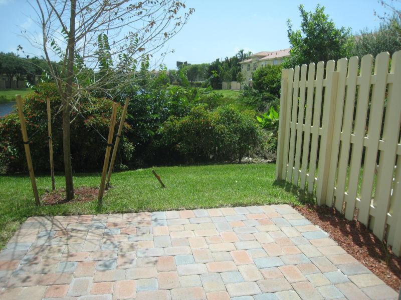 A paved patio overlooks a grassy yard, a small tree, and a white picket fence — 138 Monterey Bay Drive, Boynton Beach FL 33426, BOYNTON BEACH, FL