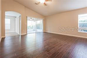 An empty living room features dark wood-look flooring, a vaulted ceiling, and sliding glass doors — 29636 TEE SHOT DRIVE, SAN ANTONIO, FL
