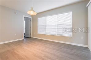 An empty room features light-colored wood-look flooring, gray walls, a window with blinds, and a pendant light — 29636 TEE SHOT DRIVE, SAN ANTONIO, FL