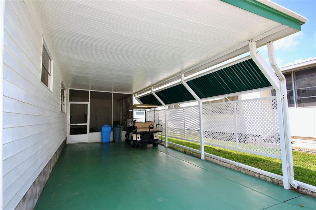 A covered carport with a green concrete floor, a golf cart, and white lattice siding — 82292 2ND AVENUE N UNIT 292, PINELLAS PARK, FL