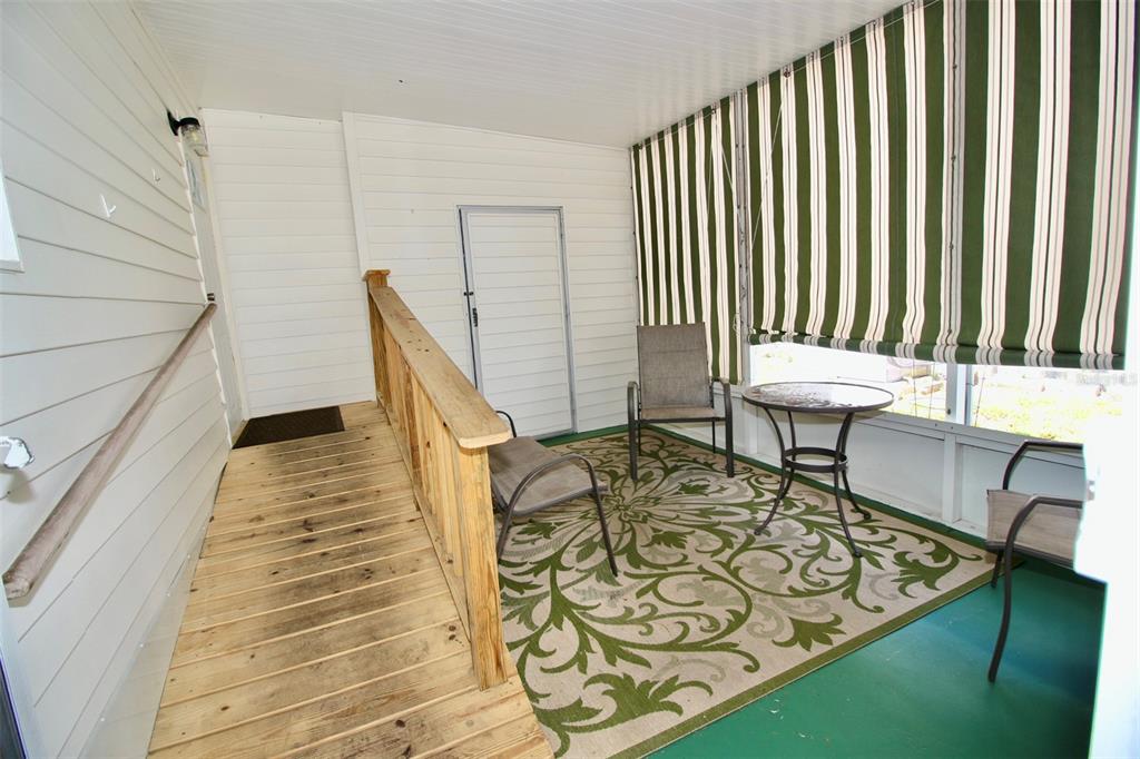 A covered porch features a wooden ramp, a patterned area rug, and green striped shades — 82292 2ND AVENUE N UNIT 292, PINELLAS PARK, FL