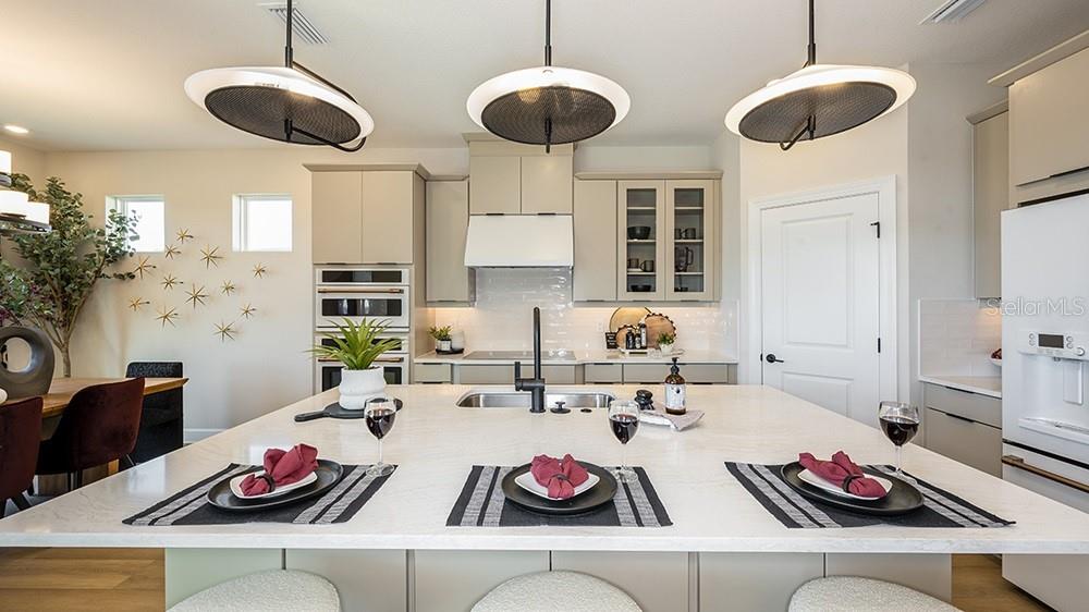 A modern kitchen features a large white island, three pendant lights, and light-colored cabinetry — 17806 SEDONA STREET, WINTER GARDEN, FL