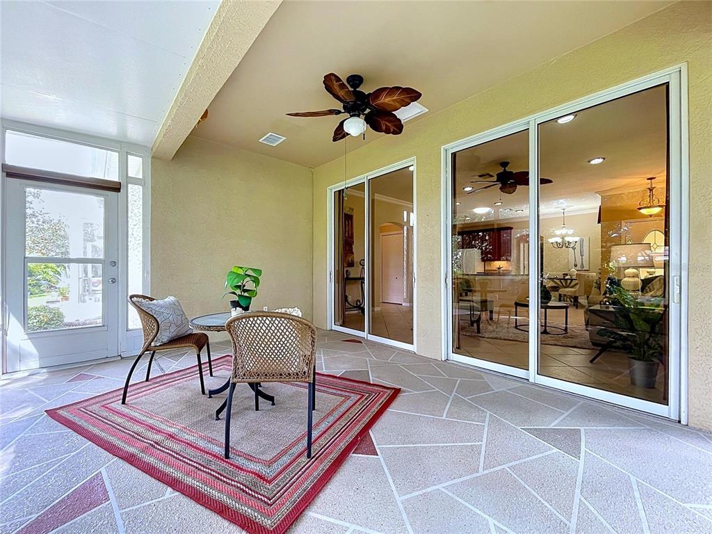 A covered patio features a patterned concrete floor, a ceiling fan, and sliding glass doors — 2018 INVERNESS GREENS DRIVE UNIT 2018, SUN CITY CENTER, FL