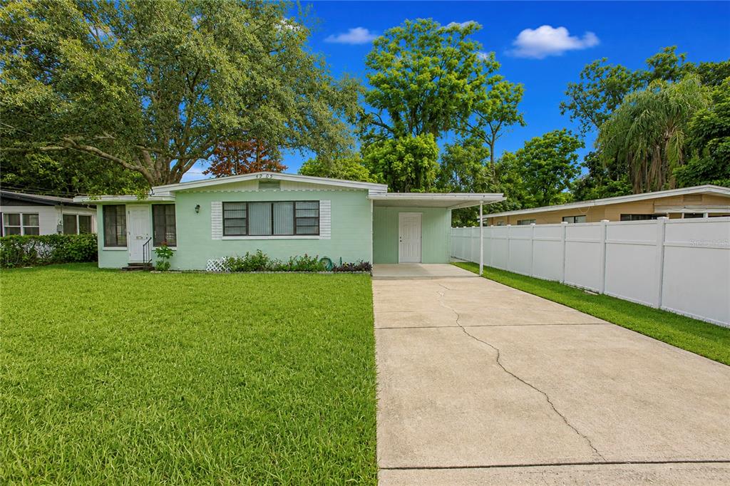 A light green single-story house features a concrete driveway, a carport, and a white fence — 4205 MIZELL STREET, ORLANDO, FL