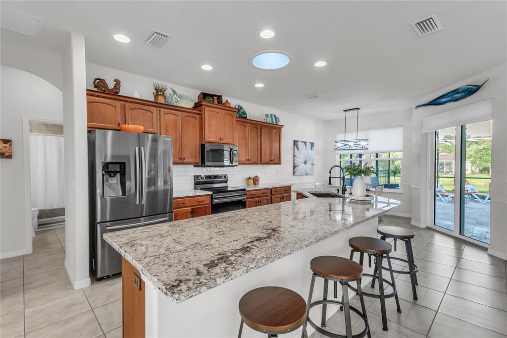 A kitchen features wood cabinets, granite countertops, a large island with stools, and tile flooring — 113 ARENA LAKE DRIVE, PALM COAST, FL