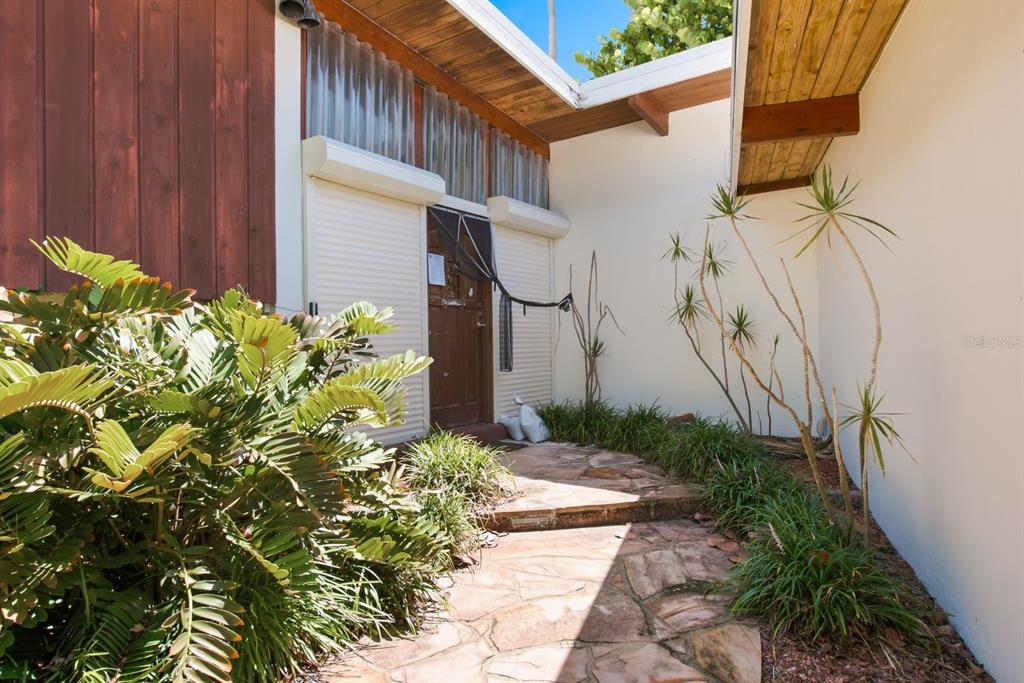 An exterior entryway features a stone path, a wooden door with shutters, and tropical landscaping — 31 DOLPHIN DRIVE, TREASURE ISLAND, FL